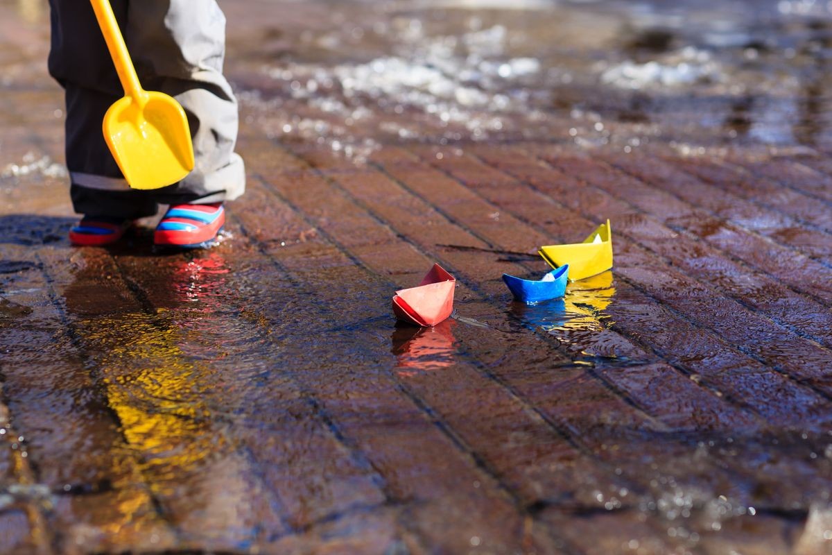 child playing with paper boats in spring puddle