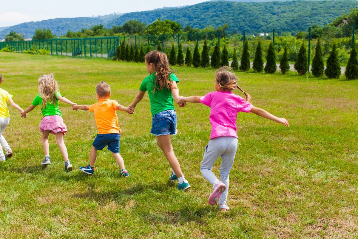 Children play holding hands on the green grass, back view
